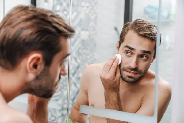 Handsome young shirtless man applying aftershave — Stock Photo, Image
