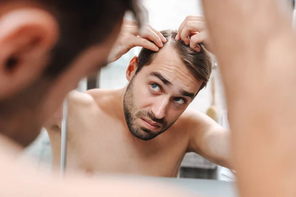 Беспокойный молодой человек без рубашки осматривает свои волосы — стоковое фото