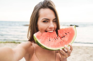 Karpuz yiyen ve selfie çeken neşeli bir kadın resmi.