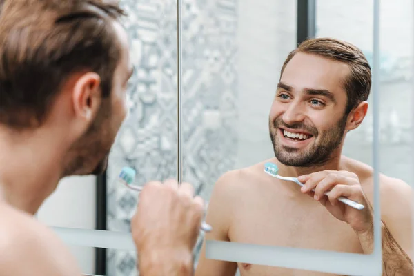 Atraktivní usmívající se muž bez košile čistí zuby — Stock fotografie