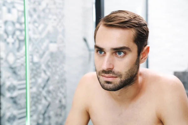 Feliz jovem sem camisa homem olhando para si mesmo no banheiro — Fotografia de Stock