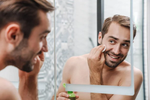 Guapo joven sin camisa hombre aplicando aftershave —  Fotos de Stock