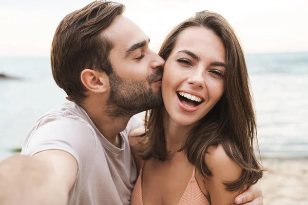 행복 한 젊은 남자가 셀카를 먹으면서 여자에게 키스하고 껴안는 모습 — 스톡 사진