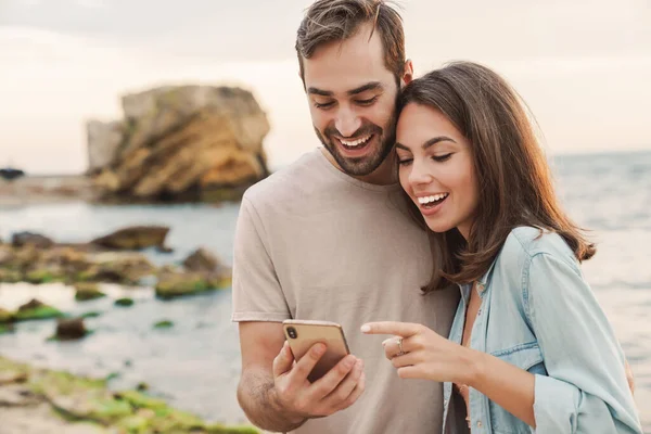 Foto van opgewonden jong paar met behulp van en wijzende vinger naar mobiele telefoon — Stockfoto