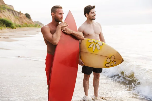 Positivo dos hombres surfistas amigos con surfings en una playa —  Fotos de Stock