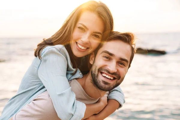 Bild von jungen glücklichen Mann gibt huckepack Fahrt schöne Frau — Stockfoto