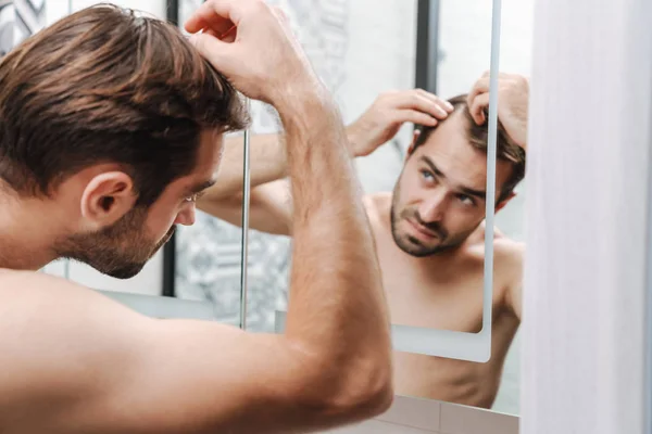 Hombre joven sin camisa preocupado examinando su cabello — Foto de Stock