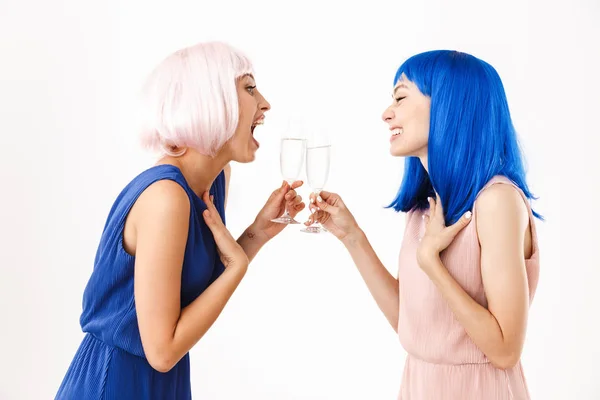 Retrato de duas mulheres surpresas vestindo perucas azuis e rosa falando enquanto bebem champanhe — Fotografia de Stock