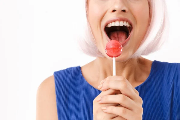 Retrato recortado de una joven sorprendida con peluca rosa sosteniendo piruleta y riéndose de la cámara — Foto de Stock