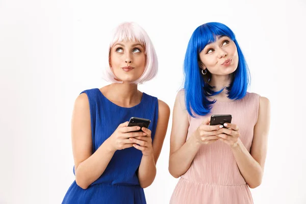 Két elégedett nő portréja, akik kék és rózsaszín parókát viselnek, felfelé néznek, miközben mobiltelefonokat tartanak a kezükben. — Stock Fotó