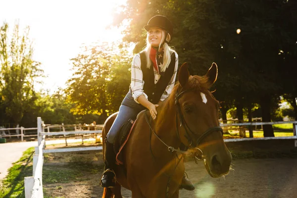 Imagen de mujer rubia con sombrero a caballo en el patio en countr —  Fotos de Stock