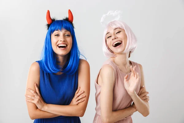 Ritratto di due belle giovani donne che indossano corna del diavolo giocattolo e aureola guardando e ridendo della macchina fotografica — Foto Stock