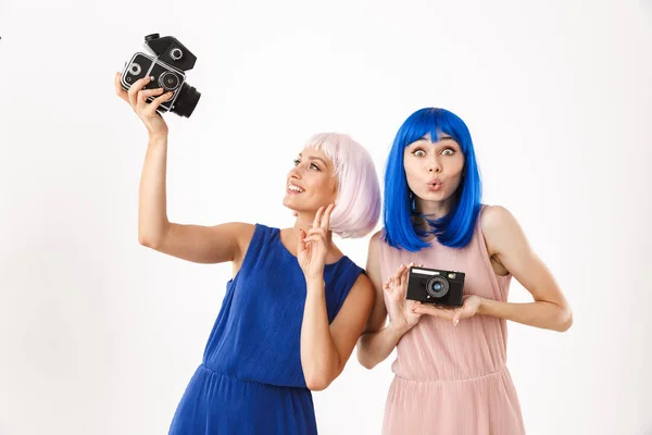 Portret van twee vrolijke vrouwen die blauwe en roze pruiken dragen die een vredesgebaar maken terwijl ze retro camera 's gebruiken — Stockfoto