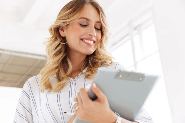 Image of joyful secretary woman smiling and holding clipboard in — Stock Photo, Image