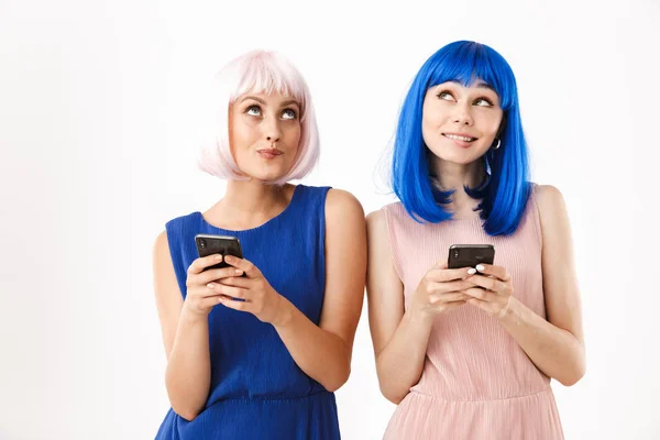 Portré két álmodozó nőről kék és rózsaszín parókában, akik felfelé néznek, miközben mobiltelefonokat tartanak a kezükben. — Stock Fotó