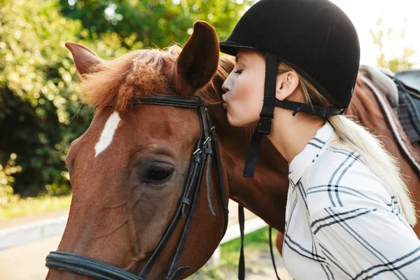 一个娇嫩的女人头戴礼帽在院子里亲吻马的照片 — 图库照片