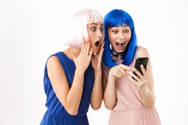 Két megdöbbent nő portréja kék és rózsaszín parókában, akik ujjal mutogatnak és mobiltelefonokat néznek. — Stock Fotó