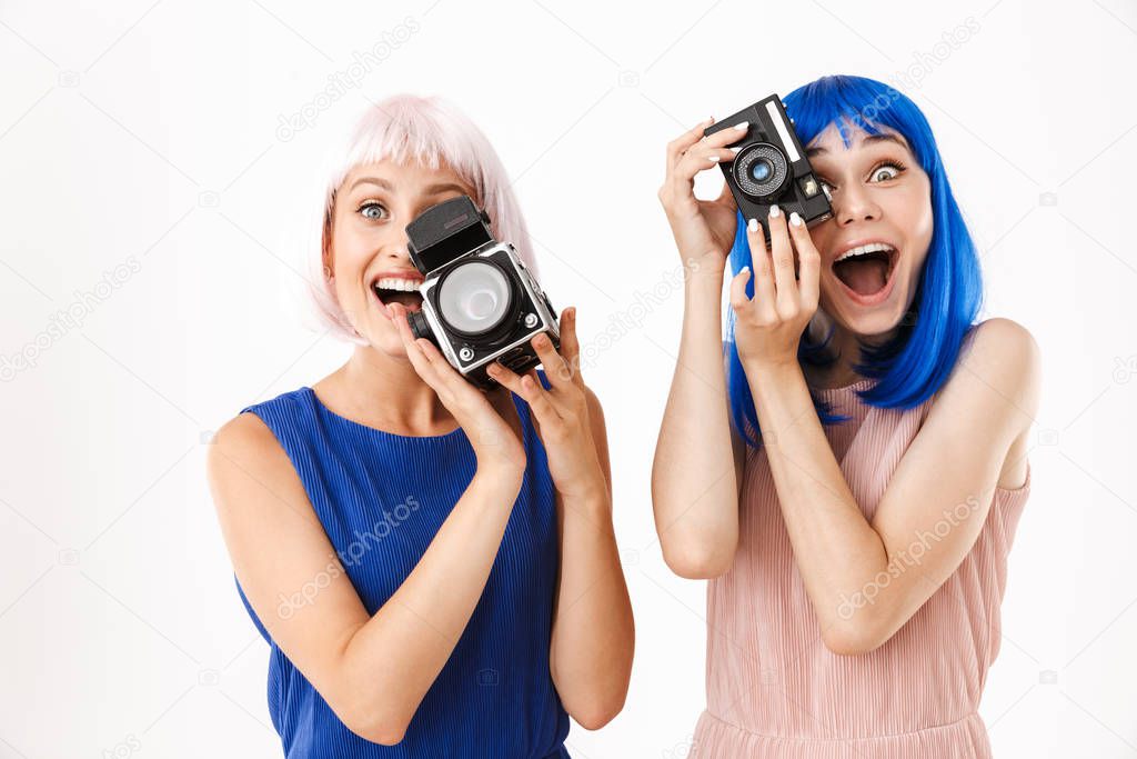 Portrait of two amazed women wearing blue and pink wigs taking photo on retro cameras