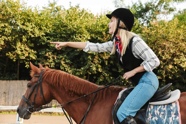 Imagen de la mujer que lleva sombrero señalando el dedo mientras monta a caballo en —  Fotos de Stock