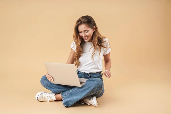 Imagen de una mujer sonriente usando un portátil de plata mientras está sentada en el suelo — Foto de Stock