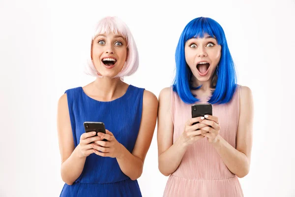 Portré két eksztatikus nő kék és rózsaszín parókát visel, amint a kamerába néznek, miközben mobilon gépelnek. — Stock Fotó