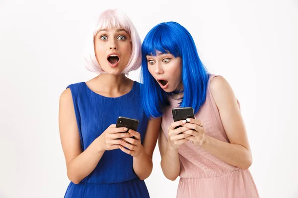 Két megdöbbent nő portréja kék és rózsaszín parókában, akik mobiltelefonokat nézegetnek. — Stock Fotó