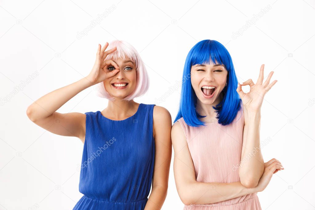 Portrait of two smiling women wearing blue and pink wigs winking while gesturing ok sign