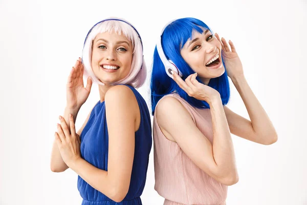 青とピンクのウィッグを身に着けている2人の幸せな女性の肖像｜ヘッドフォンで音楽を聴く — ストック写真