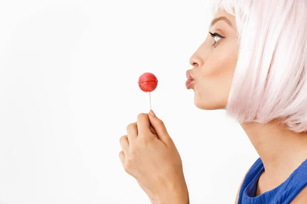 Foto no perfil de mulher feliz alegre vestindo peruca rosa segurando pirulito e fazendo rosto beijo — Fotografia de Stock