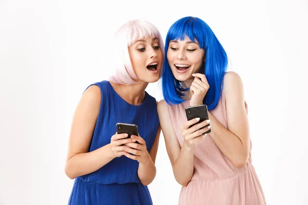 Két elképedt, kék és rózsaszín parókát viselő nő portréja, akik egymás mobilját nézik. — Stock Fotó