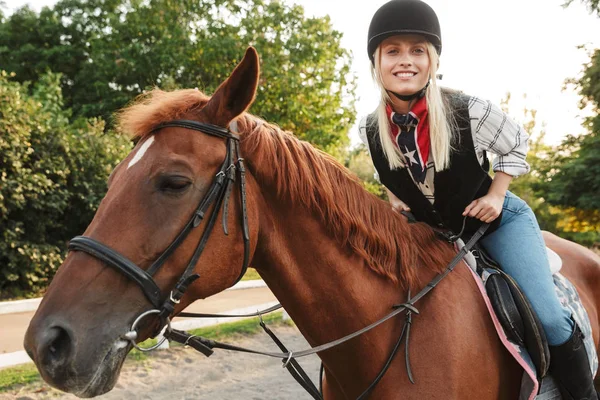 Изображение милой женщины в шляпе верхом на лошади во дворе в графстве — стоковое фото