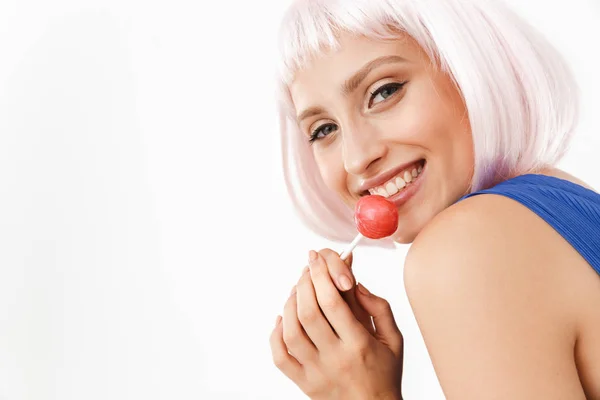 Foto de mujer feliz seductora con peluca rosa lamiendo piruleta y sonriendo a la cámara —  Fotos de Stock