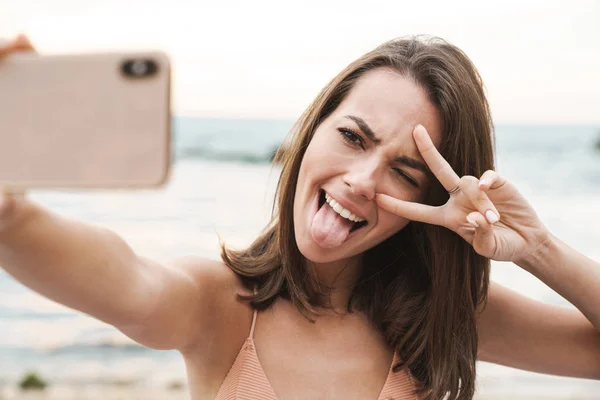 Imagen de una mujer haciendo gestos de señal de paz y tomando selfie en el teléfono celular —  Fotos de Stock