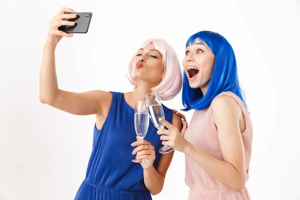 两个身穿蓝色和粉色假发的快乐女人一边喝香槟一边用手机拍照的肖像 — 图库照片