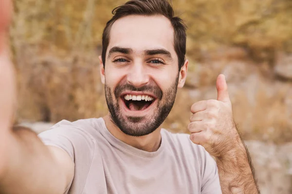 Image of unshaven laughing man showing thumb up and taking selfie photo — Stock Photo, Image