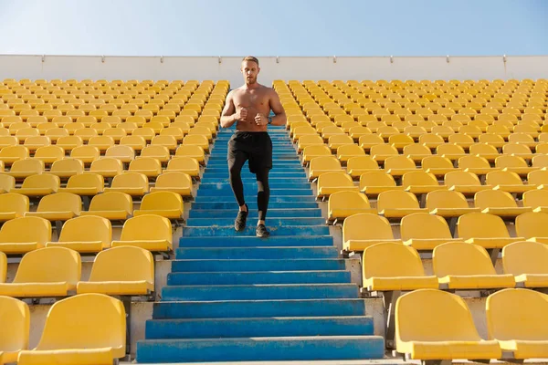 Imagen del deportista musculoso corriendo por los asientos del estadio mientras hace — Foto de Stock
