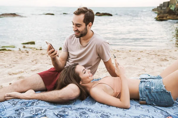 Foto di allegra giovane coppia utilizzando i telefoni cellulari e sorridente — Foto Stock