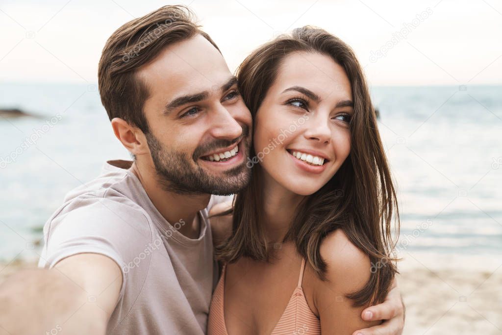 Photo of smiling young couple hugging and taking selfie photo