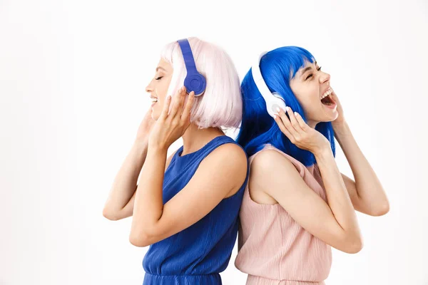 Portrait of two smiling women wearing blue and pink wigs singing while listening music with headphones — Stock Photo, Image