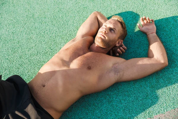 Obrázek mladého muže bez trička ležícího na zeleném sportovním hřišti outdoo — Stock fotografie