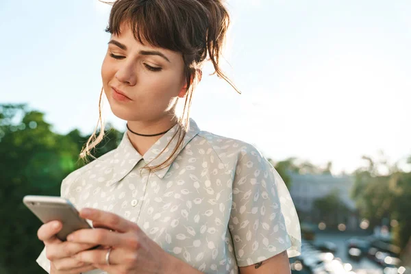 Young confused thinking pretty woman on a balcony using mobile phone chatting. — Stock Photo, Image