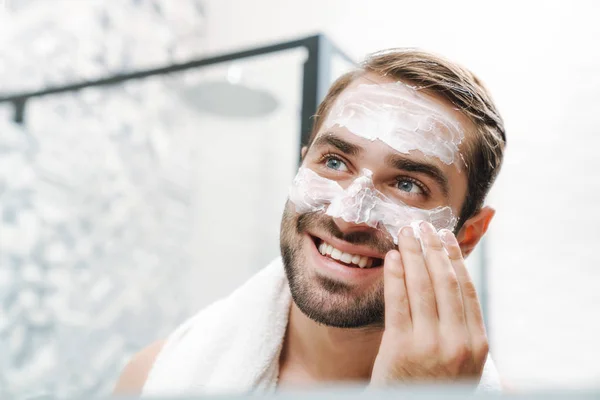 Attraente giovane uomo senza camicia che applica la crema per il viso — Foto Stock