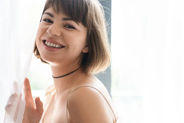 Glücklich fröhlich schöne junge Frau posiert drinnen zu Hause in der Nähe Fenster mit Vorhang. — Stockfoto