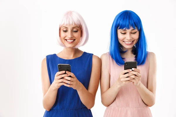 Két boldog nő portréja, kék és rózsaszín parókát viselnek, mosolyognak, miközben mobilon gépelnek. — Stock Fotó