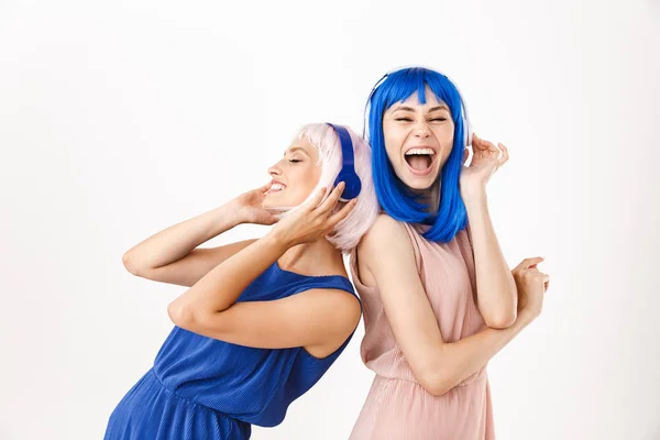 Porträtt av två leende kvinnor i blå och rosa peruker lyssna musik med hörlurar — Stockfoto