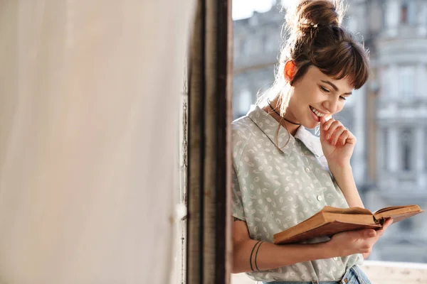 Χαριτωμένη νεαρή όμορφη γυναίκα διαβάζει το βιβλίο σε ένα μπαλκόνι. — Φωτογραφία Αρχείου