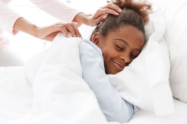 Uyuyan kızını örten Afrikalı Amerikalı bir kadın.