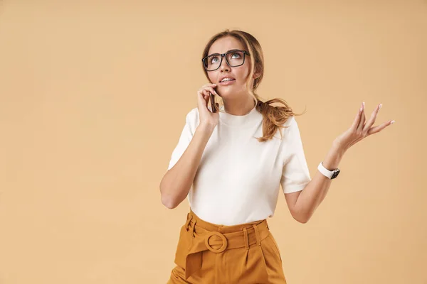 Imagen de una joven desconcertada que usa anteojos hablando en un teléfono inteligente — Foto de Stock