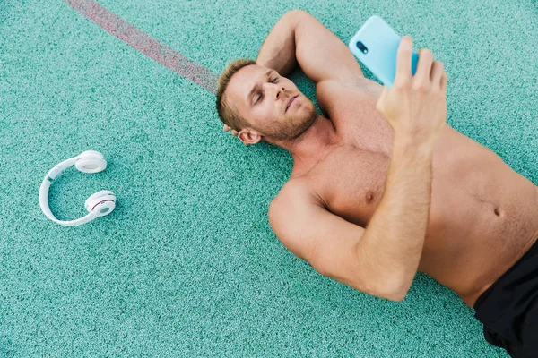 Image of shirtless man holding smartphone while lying at sports — Stock Photo, Image