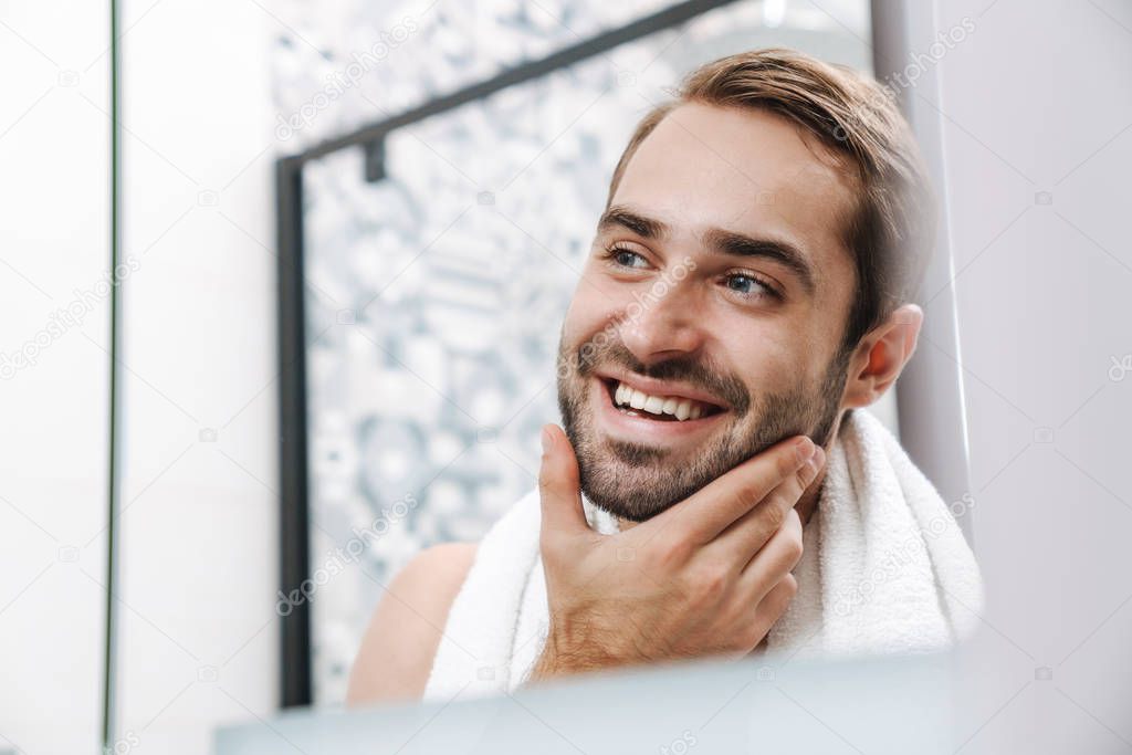 Happy young shirtless man looking at himself at the bathroom